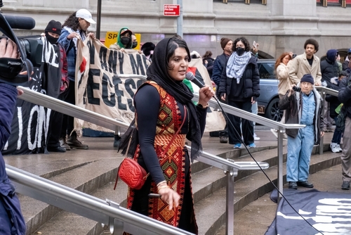 A woman speaking at a protest with banners in the background