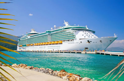shutterstock_536760823.jpg Large cruise ship docked near turquoise water and foliage.