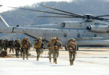 Soldiers walk past military helicopter on airfield.