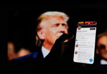Hand holding smartphone displaying Twitter profile.