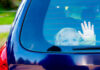 Child waving from the back window of car.