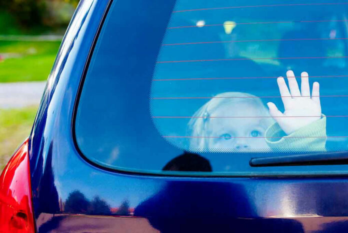 Child waving from the back window of car.