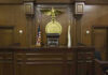 Captain Cracks Before Trial – He Did It! Judges bench in an empty courtroom, scales emblem above.