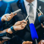 Hollywood Gatekeepers Caught Quietly Silencing Journalists holding microphones interview a person in a suit.