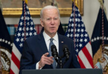 Man speaking at podium with American flags behind