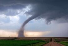 Tornado touching down over open farmland under dark storm clouds