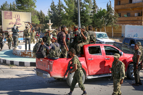 Fighters,In,The,Armed,Syrian,Opposition,Raise,The,Hands,Of Group of soldiers in military gear gathered around a red pickup truck in an urban setting