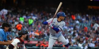 A baseball player from the Dodgers prepares to bat while the catcher is in position