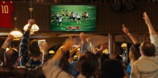 Crowd cheering in a sports bar while watching a football game on a large screen