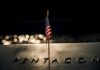 Close-up of a small American flag on a reflective surface with the word PENTAGON in the background