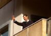A man in formal attire waving from a balcony