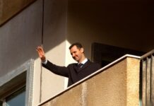 Bomb Blasts Jolt Macron’s Damascus Gamble A man in formal attire waving from a balcony