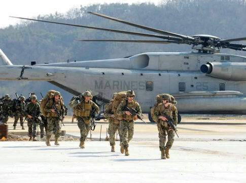Soldiers walk past military helicopter on airfield.
