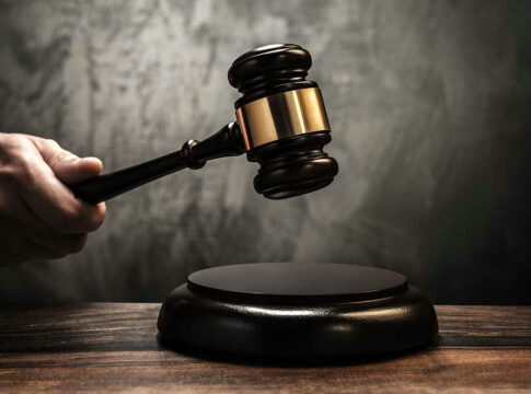 Hand holding judges gavel over sounding block.