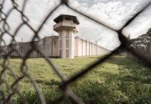 Watchtower and prison fence viewed through chain-link fence.