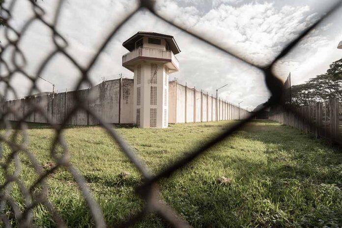 Watchtower and prison fence viewed through chain-link fence.