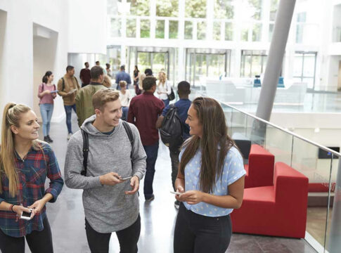 Students conversing in bright school hallway.