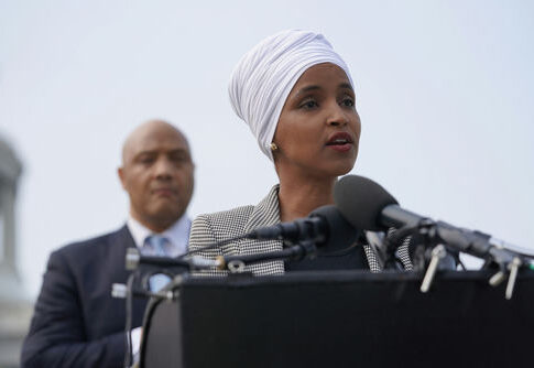 Woman in white headwrap speaking at podium with microphones