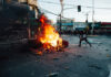 Person near large street fire during protest.