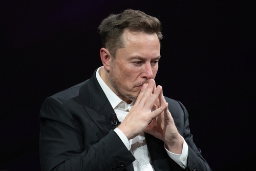 Elon Musk deep in thought, hands clasped near face.