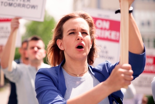 Protesters hold signs and chant during a daytime rally.