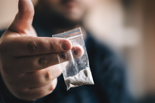 Person holding a small bag of white powder.